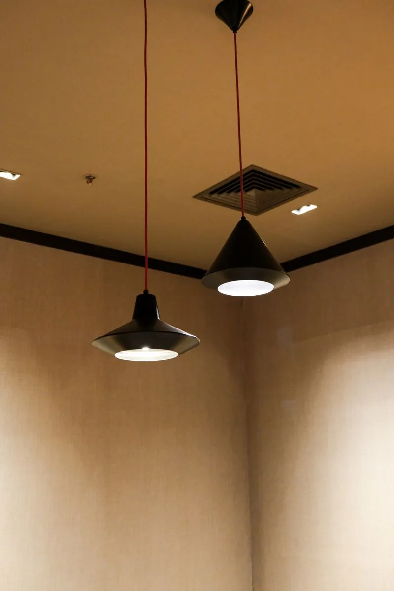 Two black conical pendant lamps on red flex, lit against a warm fabric-panelled wall